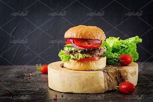 عکس همبرگر روی تخته چوب کنار سبزیجات